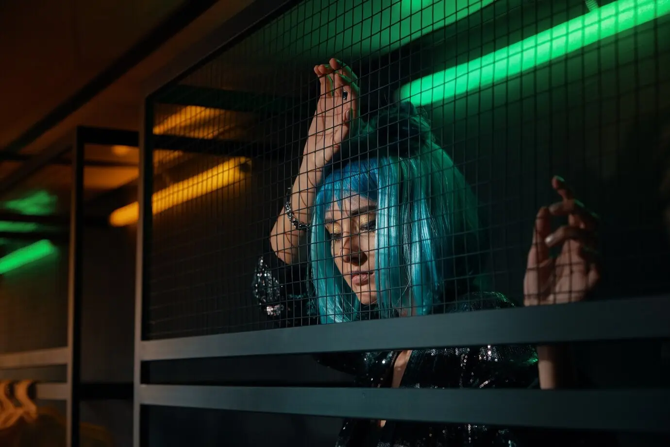 За металлической проволочной сеткой стоит девушка.