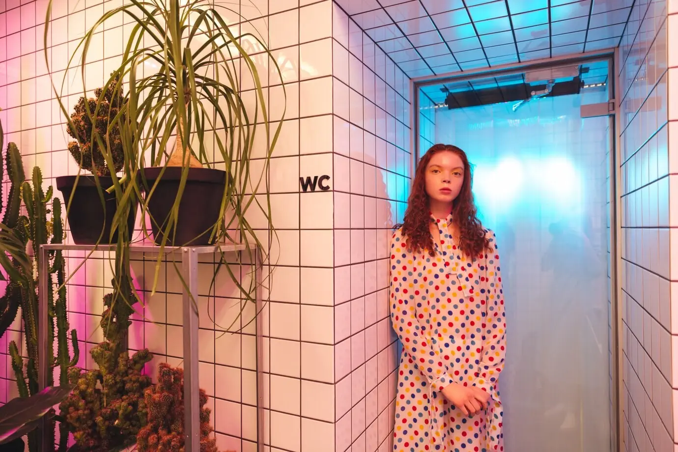 Серьёзная молодая рыжеволосая кудрявая женщина стоит в кафе рядом с туалетом.